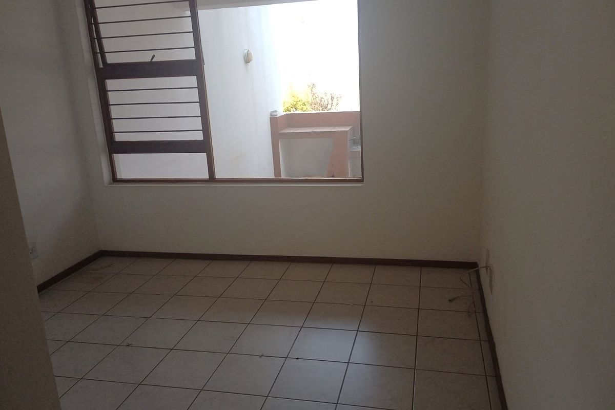 An empty bedroom featuring tiled flooring and a large window overlooking an outdoor area, providing a blank canvas for potential interior design.