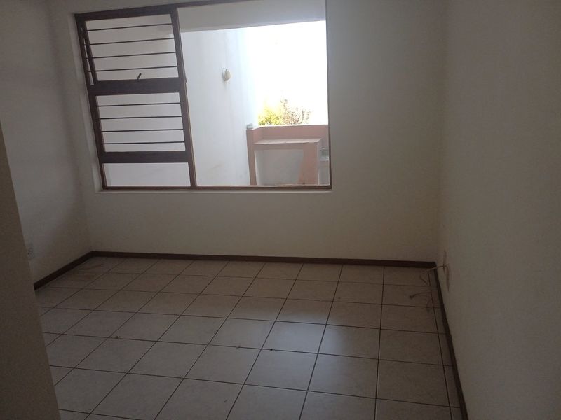 An empty bedroom featuring tiled flooring and a large window overlooking an outdoor area, providing a blank canvas for potential interior design.
