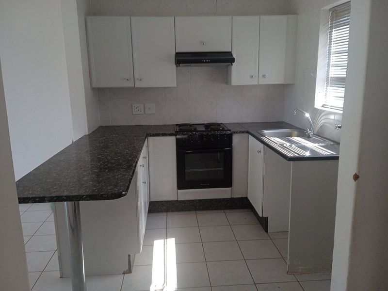 A functional kitchen featuring white cabinetry, granite countertops, a built-in oven with extractor fan, and a breakfast bar, finished with tiled flooring.