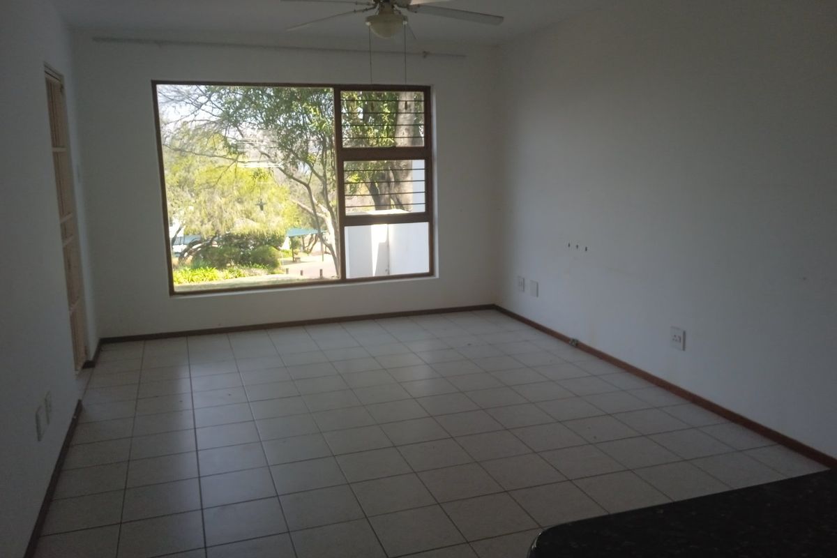 An empty living room featuring tiled flooring, a ceiling fan, and a large window providing natural light and garden views.