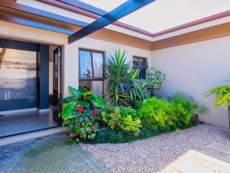 A well-maintained covered patio area featuring a modern pergola, paved flooring, and landscaped garden beds with gravel accents.