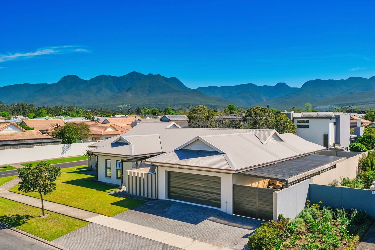 Aerial view of a modern residential property featuring a metal roof, double garage, paved driveway, and well-maintained garden with mountain views.