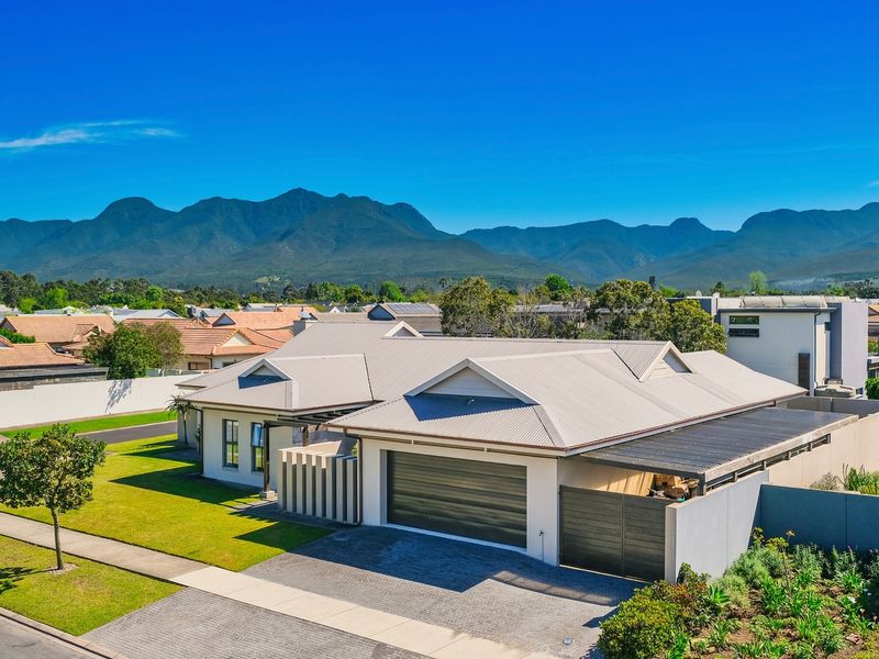 Aerial view of a modern residential property featuring a metal roof, double garage, paved driveway, and well-maintained garden with mountain views.