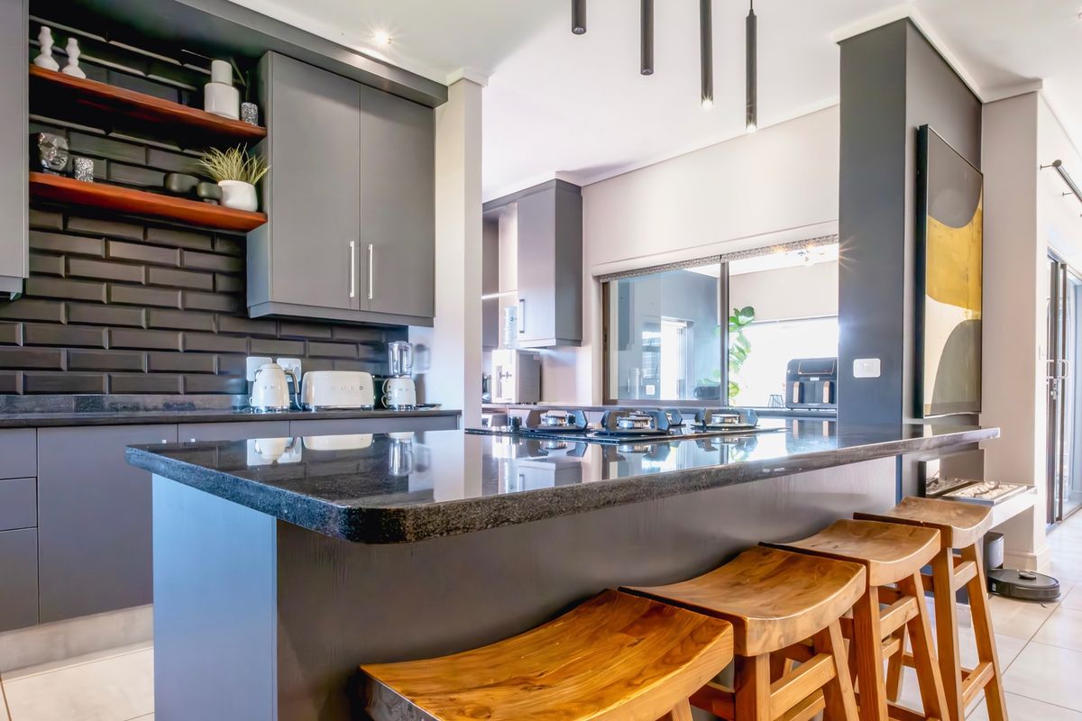 Modern kitchen featuring dark cabinetry, granite countertops, a gas hob, and stylish subway tile backsplash with integrated floating shelving.