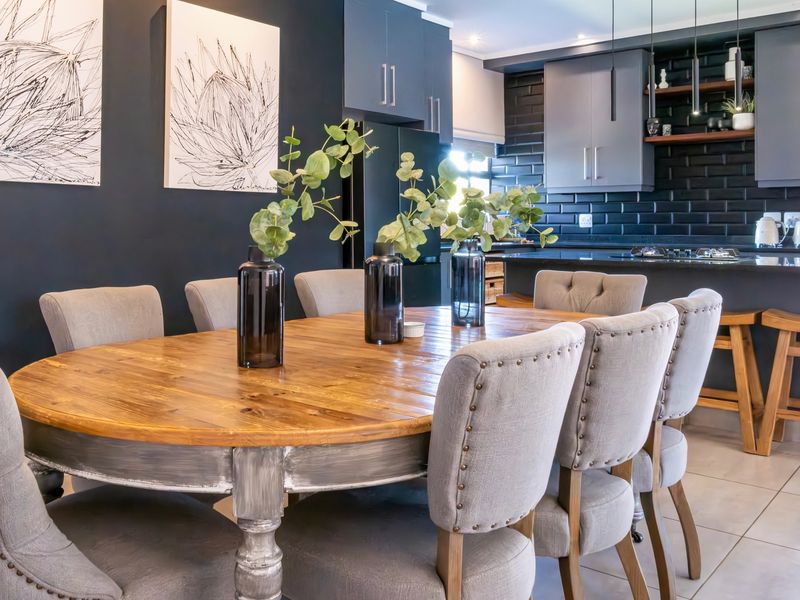 Modern open-plan kitchen and dining area featuring dark cabinetry, a subway tile backsplash, kitchen island with hob, and contemporary pendant lighting.
