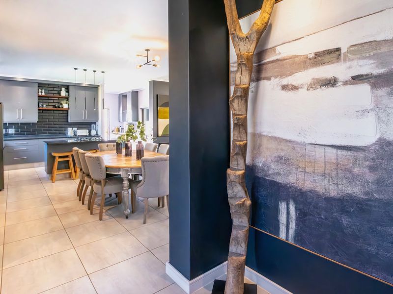 Modern open-plan living area featuring a contemporary kitchen with dark cabinetry, a central island, and neutral tiled flooring throughout the dining and kitchen space.