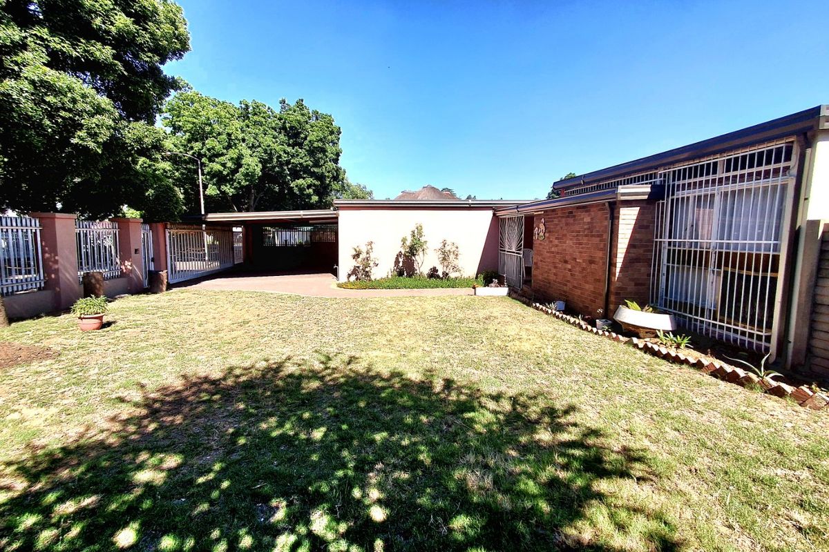 Rear view of the property featuring a brick facade, security bars on windows, a carport, and a spacious lawn area.