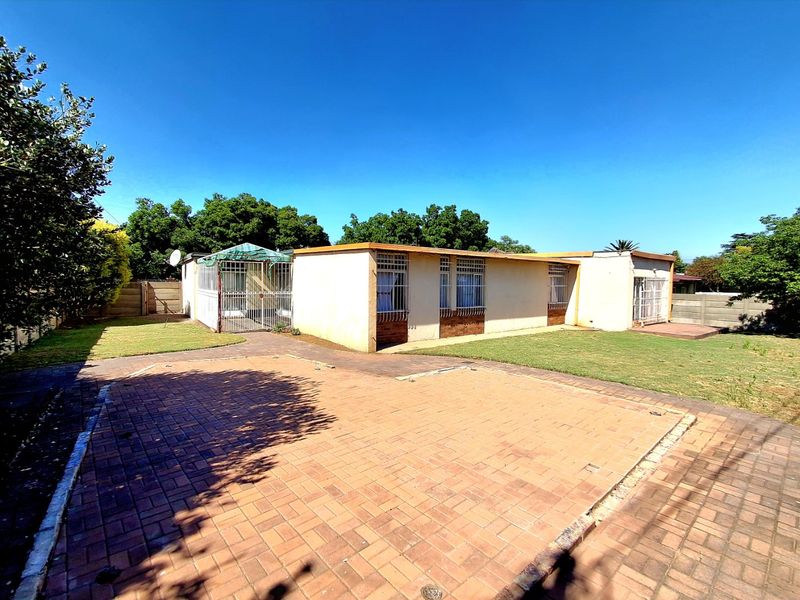 Rear view of the property featuring a paved driveway, lawn area, and a covered patio with security bars on the windows.