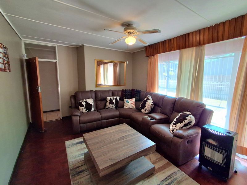 A comfortable living room featuring dark wood flooring, a ceiling fan, and large windows fitted with security bars and a decorative timber pelmet.
