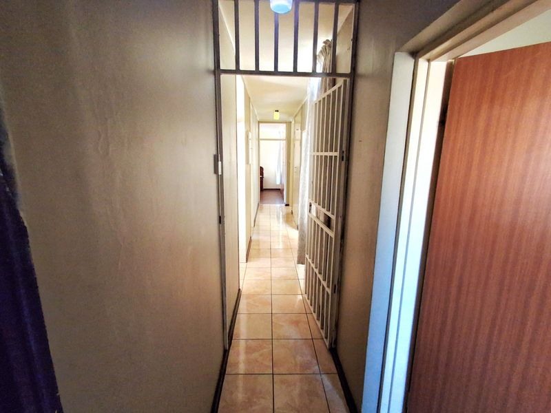 A narrow residential hallway featuring tiled flooring and a built-in security gate, providing access to multiple rooms within the property.
