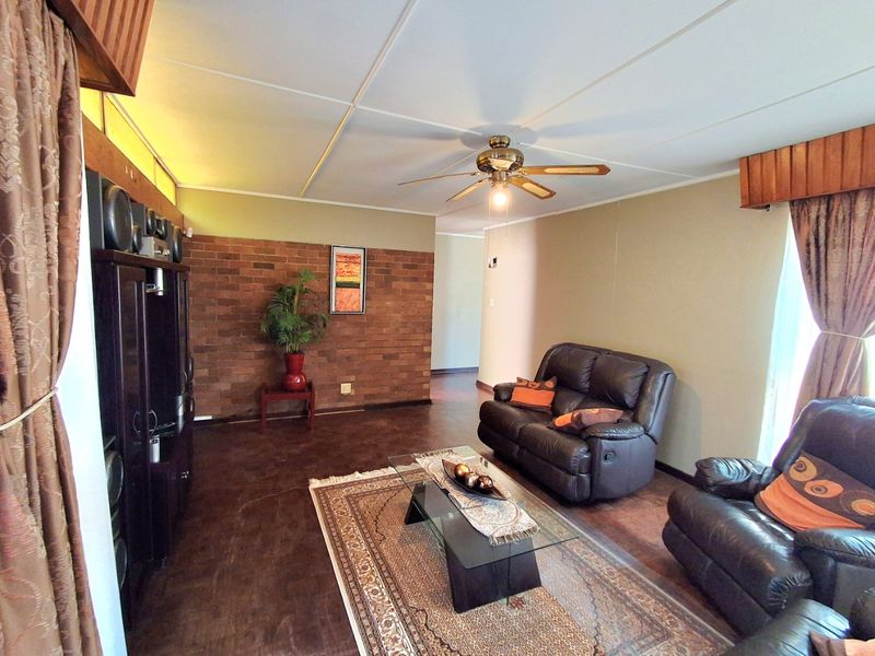 A living room featuring an exposed brick accent wall, tiled flooring, and a ceiling fan, offering a dated but functional living space.
