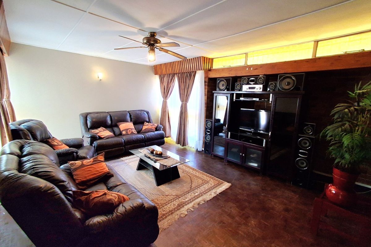 A spacious living room featuring parquet flooring, a ceiling fan, and timber wall paneling with clerestory windows providing natural light.