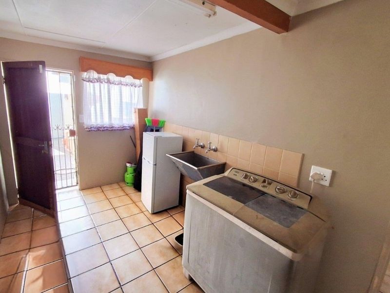 Functional laundry area featuring a stainless steel wash trough, tiled splashback, and direct access to the exterior via a security gate.