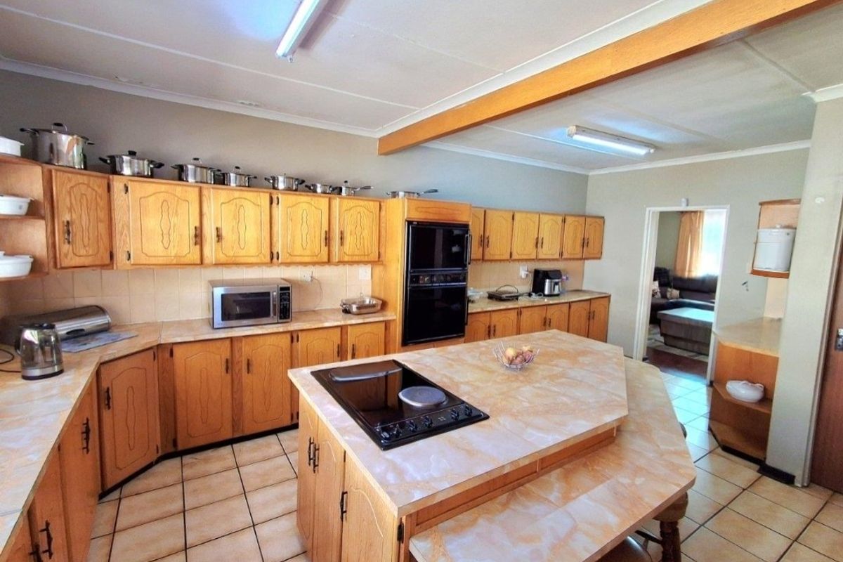 Spacious kitchen featuring extensive wooden cabinetry, a central island with a built-in hob, and tiled flooring, offering a functional layout with potential for modernization.