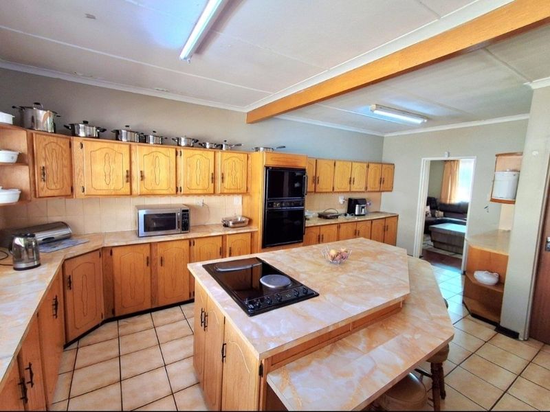 Spacious kitchen featuring extensive wooden cabinetry, a central island with a built-in hob, and tiled flooring, offering a functional layout with potential for modernization.