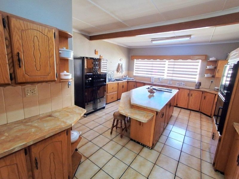 Spacious kitchen featuring extensive wooden cabinetry, a central island with breakfast bar, tiled flooring, and ample counter space for meal preparation.