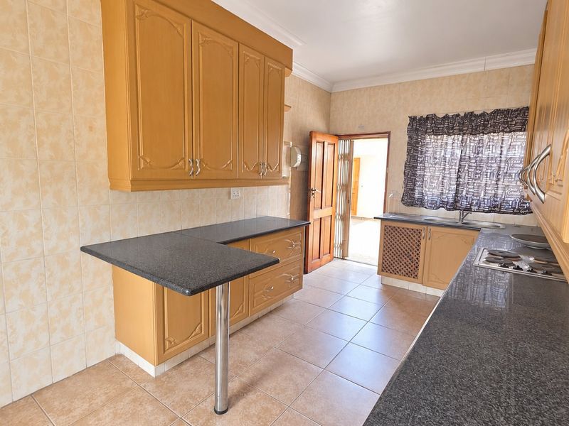 A functional kitchen featuring dated wooden cabinetry, granite countertops, a breakfast bar, and tiled flooring with direct access to an outdoor area.