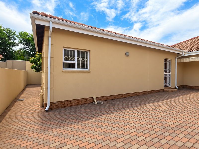 A well-maintained rear exterior view of the apartment featuring brick paving, secure window bars, and a clean rendered facade.