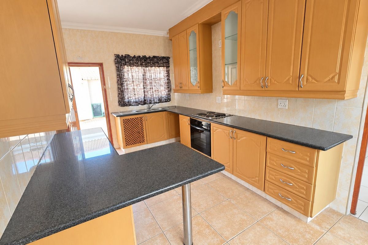 A functional kitchen featuring light wood cabinetry, dark granite countertops, built-in oven and hob, and tiled flooring with direct access to an outdoor area.