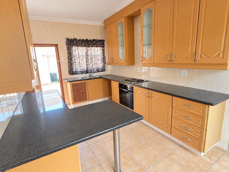 A functional kitchen featuring light wood cabinetry, dark granite countertops, built-in oven and hob, and tiled flooring with direct access to an outdoor area.