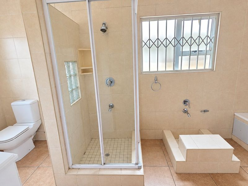 A spacious bathroom featuring a separate shower enclosure, built-in bathtub, toilet, and neutral tiled finishes throughout.