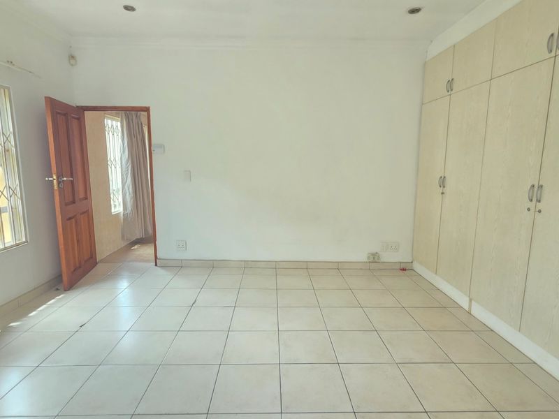 A spacious, empty bedroom featuring neutral tiled flooring, ample built-in cupboard storage, and security bars on the windows.
