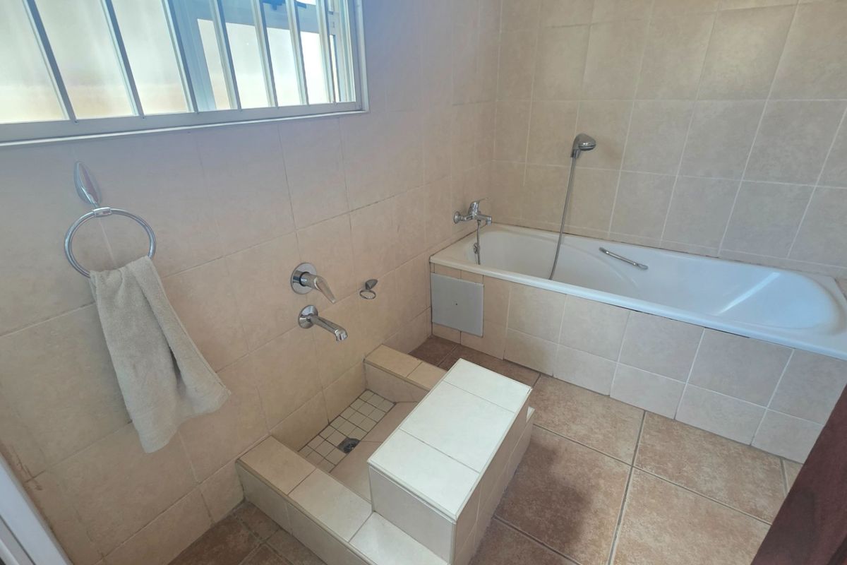 A functional bathroom featuring a built-in bathtub, tiled walls and flooring, and a dedicated foot bath area with integrated plumbing fixtures.