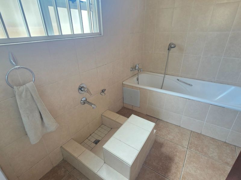 A functional bathroom featuring a built-in bathtub, tiled walls and flooring, and a dedicated foot bath area with integrated plumbing fixtures.