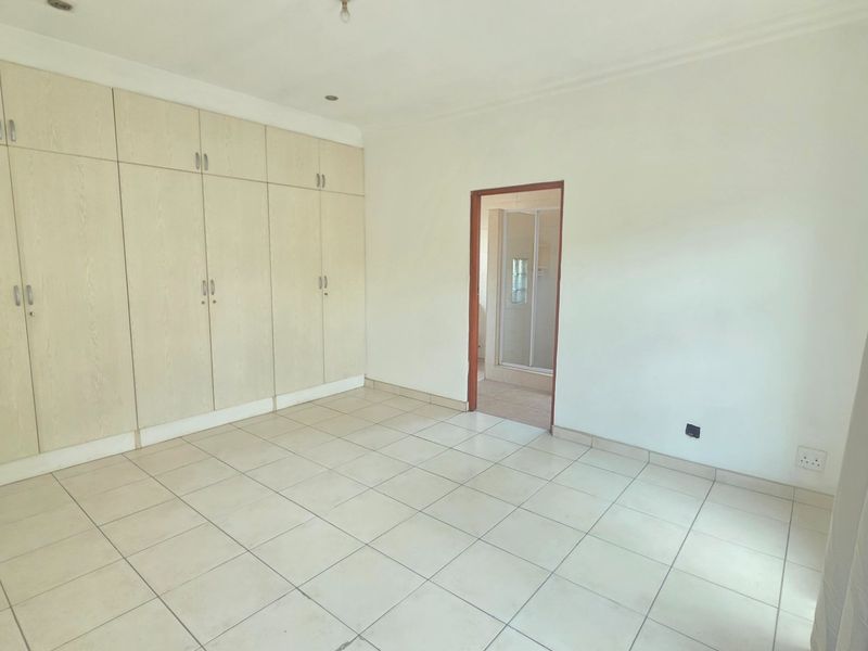 A spacious, empty bedroom featuring neutral tiled flooring and extensive built-in cupboard storage, with direct access to an en-suite bathroom.