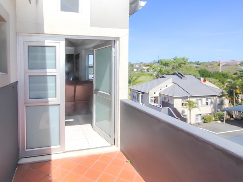 A private balcony featuring terracotta tiling and an aluminium-framed glass door, offering an elevated view of the surrounding residential complex.