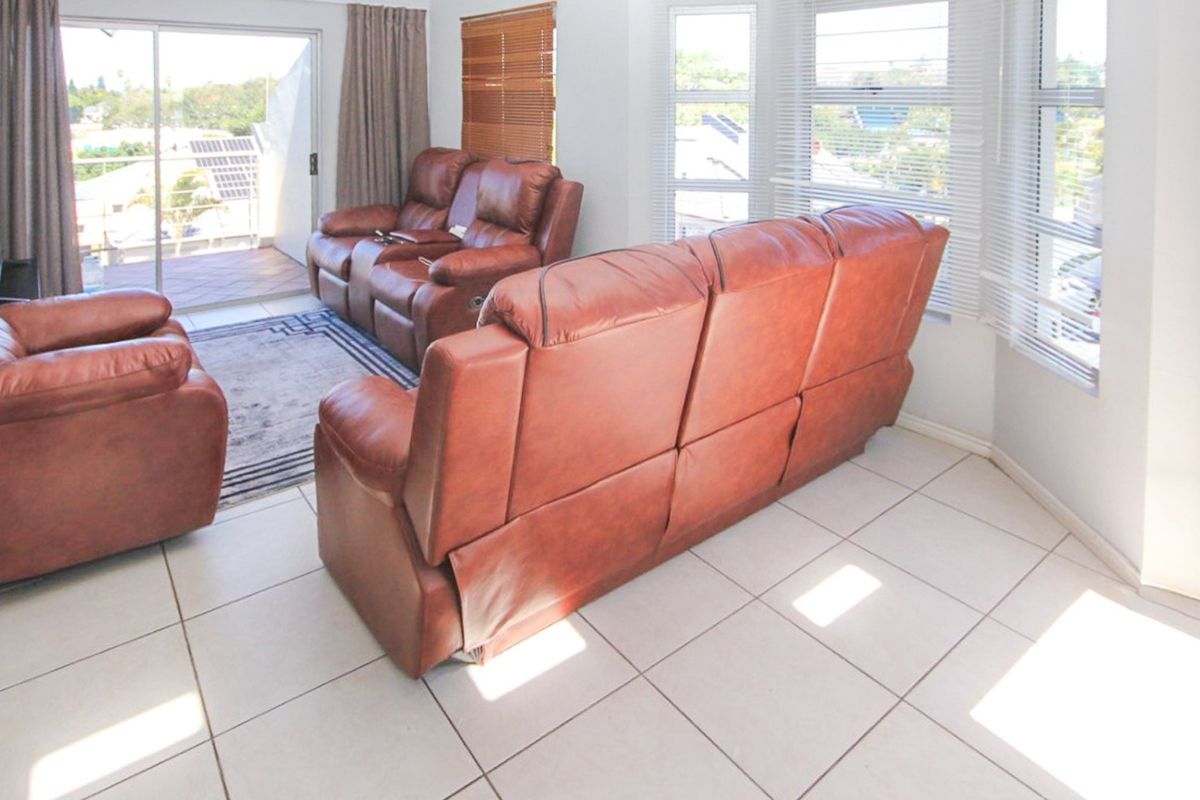 Bright living room featuring tiled flooring, large windows with venetian blinds, and direct access to an outdoor balcony through a sliding glass door.
