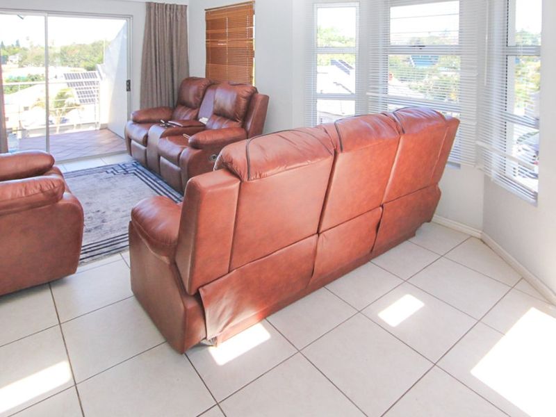 Bright living room featuring tiled flooring, large windows with venetian blinds, and direct access to an outdoor balcony through a sliding glass door.