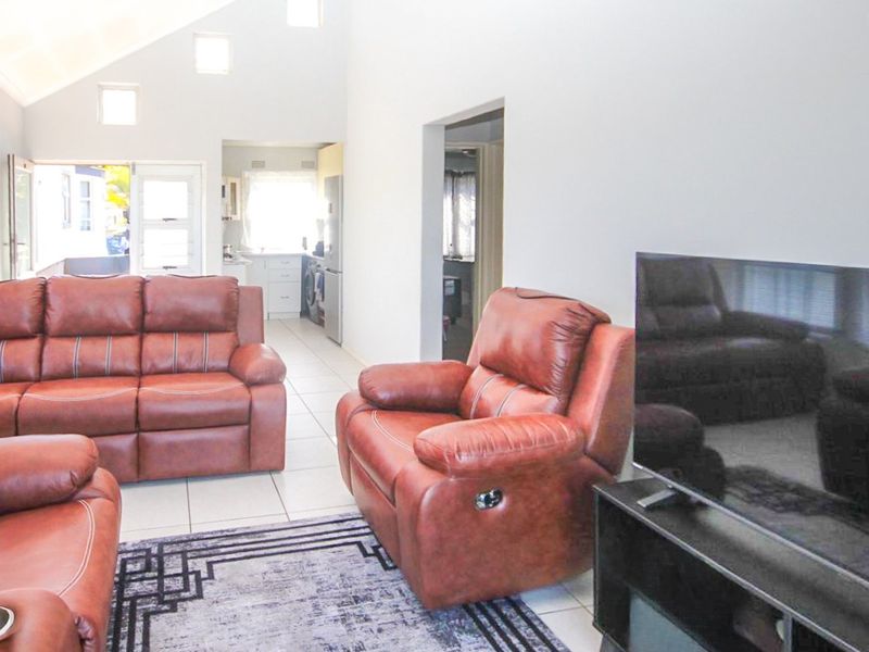 Open plan living area featuring tiled flooring, vaulted ceilings with recessed lighting, and a view through to the kitchen space.
