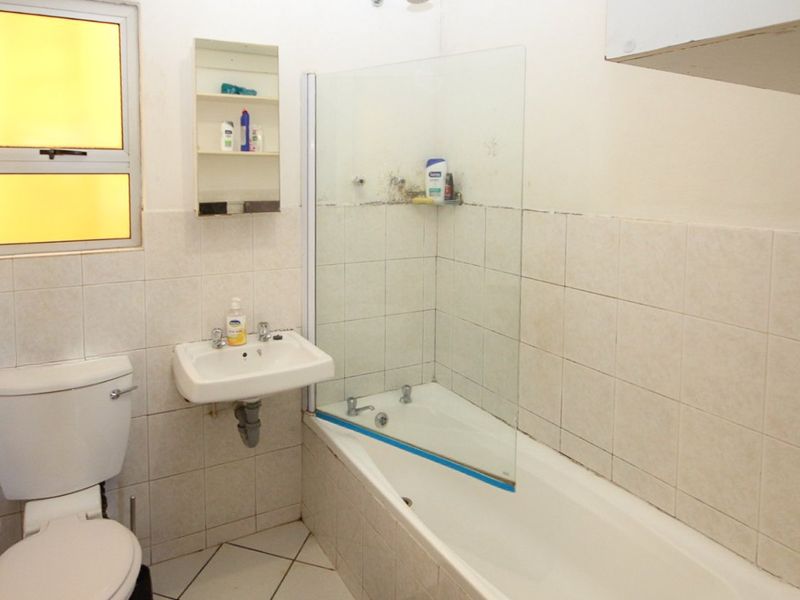 A functional bathroom featuring a wall-mounted basin, a bathtub with a glass screen, and tiled finishes throughout, requiring some cosmetic updates.