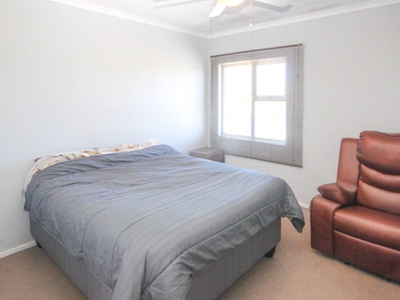 A functional bedroom featuring neutral wall tones, carpeted flooring, a ceiling fan, and a window fitted with venetian blinds.