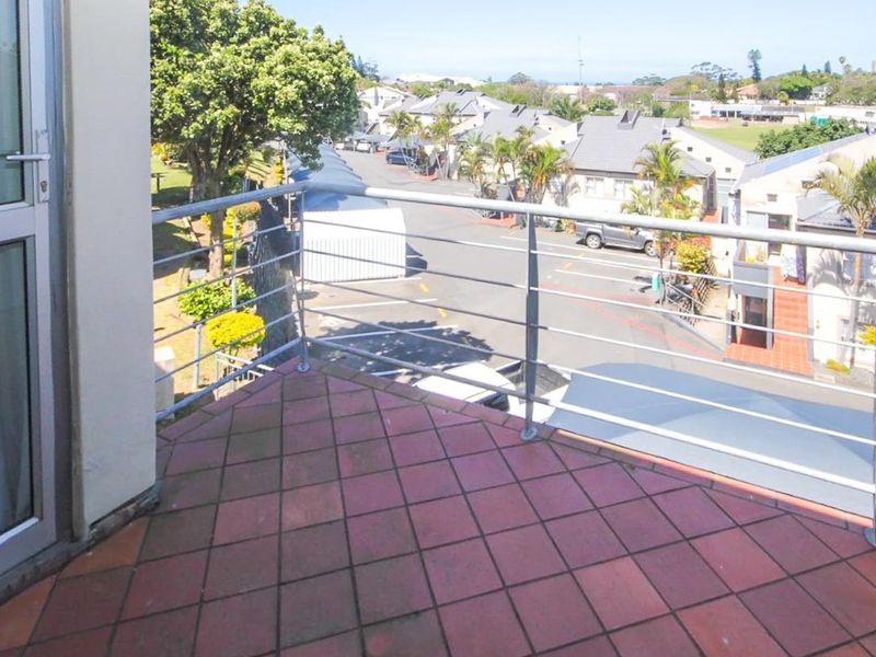 A balcony featuring tiled flooring and a metal balustrade, offering an elevated view of the surrounding residential street.