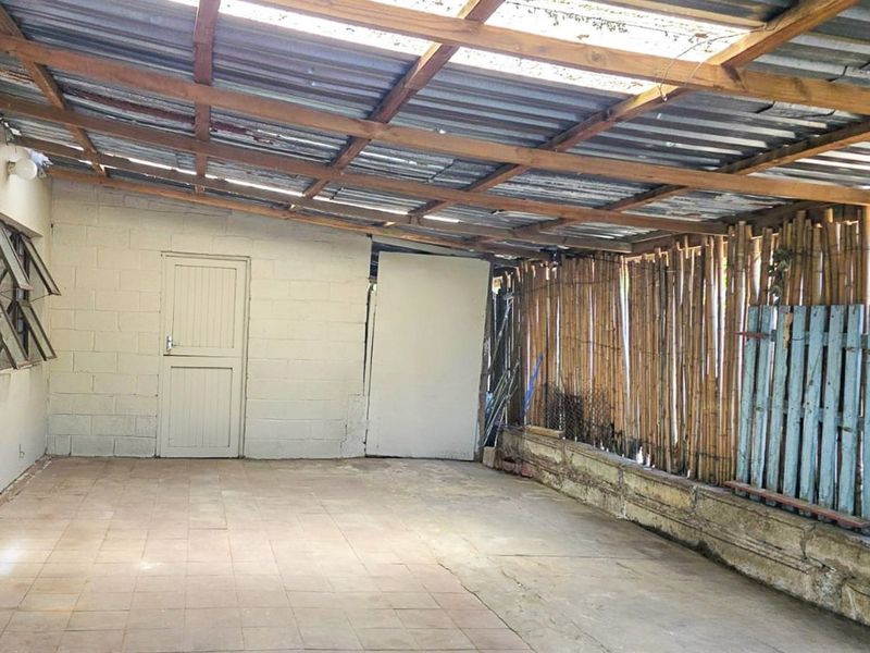 A covered outdoor patio area featuring a corrugated metal roof, tiled flooring, and a bamboo privacy screen, suitable for renovation or outdoor living space.