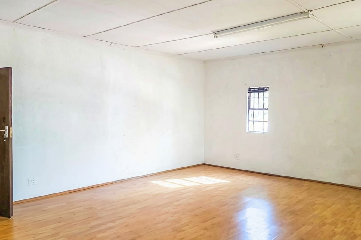 A vacant living area featuring laminate flooring, a security-barred window, and a tiled ceiling, offering a blank canvas for potential interior updates.