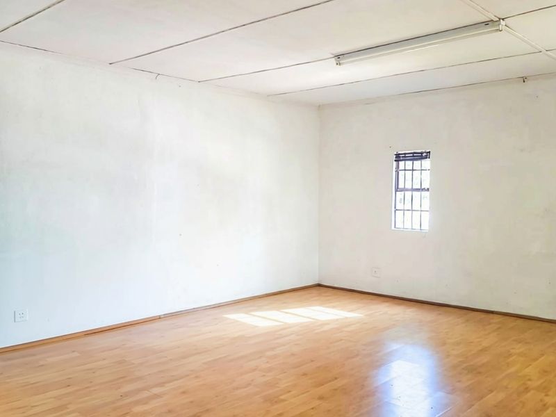 A vacant living area featuring laminate flooring, a security-barred window, and a tiled ceiling, offering a blank canvas for potential interior updates.