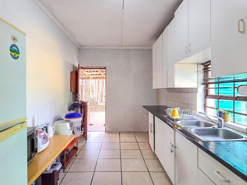A functional kitchen featuring white built-in cabinetry, a double basin sink, tiled backsplash, and direct access to an outdoor area.