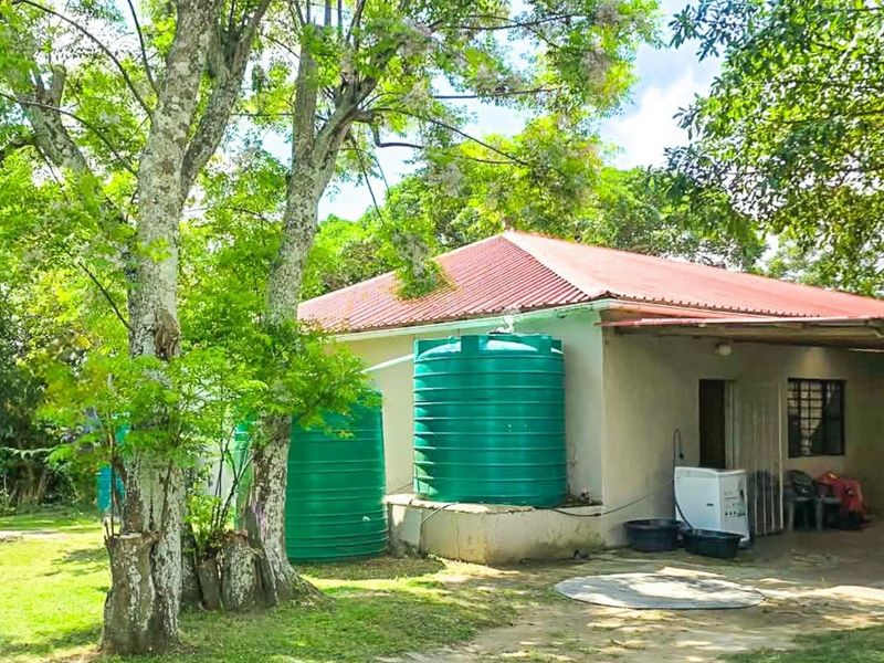 Rear view of the farm property featuring a covered carport area and external water storage tanks set within a mature garden.