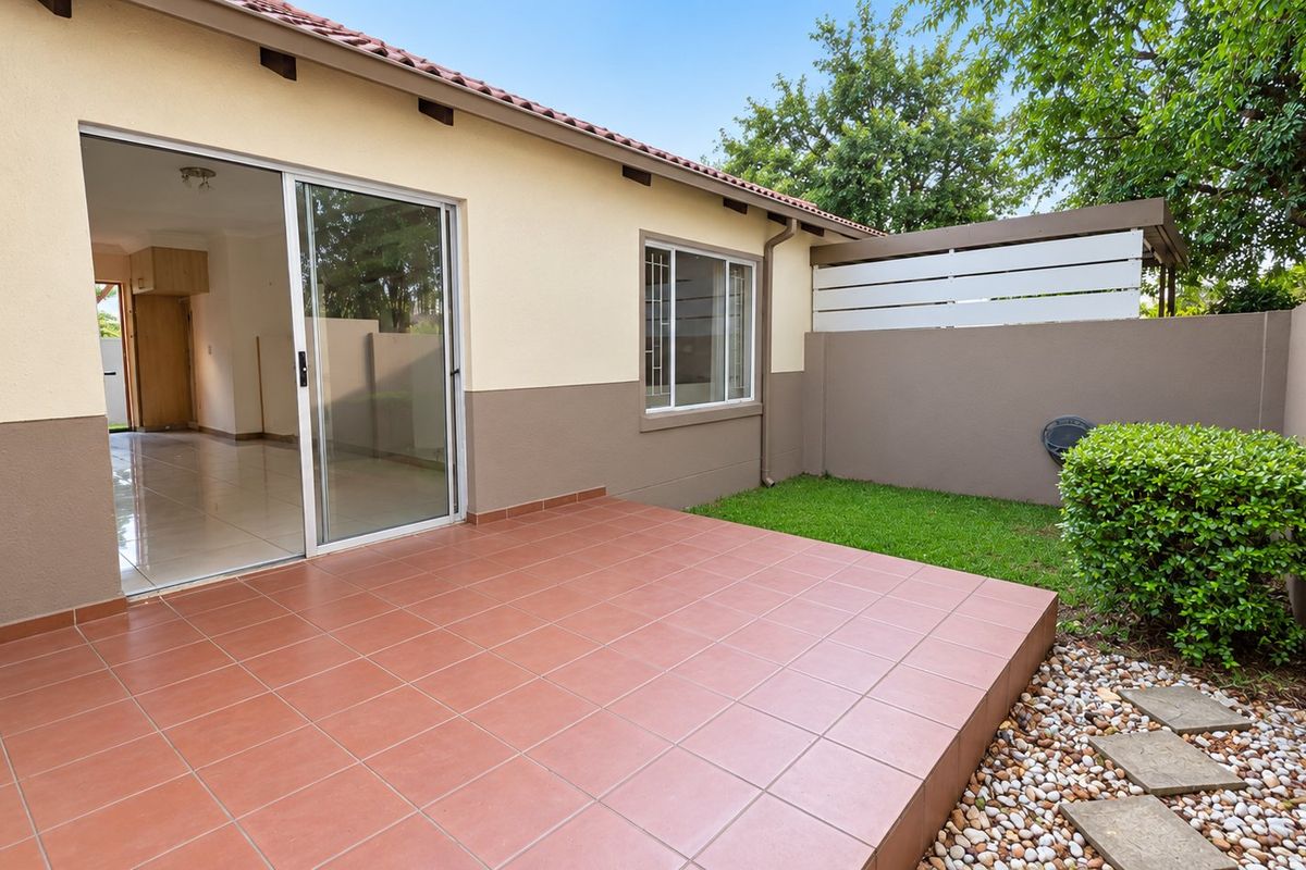 A private rear patio featuring terracotta tiling, a sliding door entrance, and a small landscaped garden area with a boundary wall.