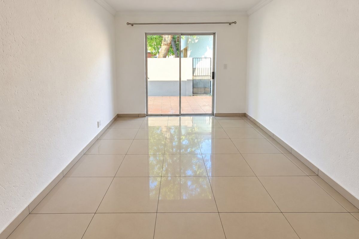 A bright, empty living room featuring neutral tiled flooring and a sliding glass door providing direct access to the outdoor patio area.