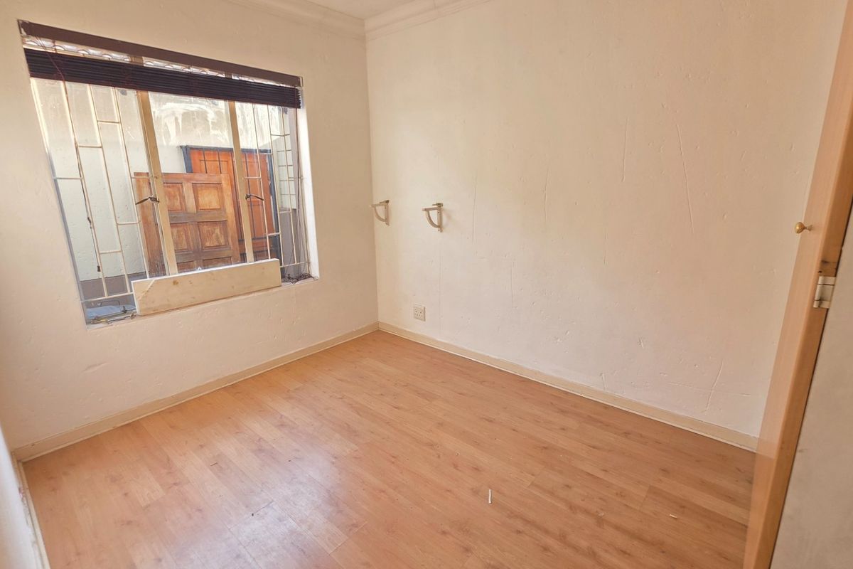 An empty bedroom featuring laminate flooring, security bars on the window, and plain white walls in need of minor cosmetic attention.