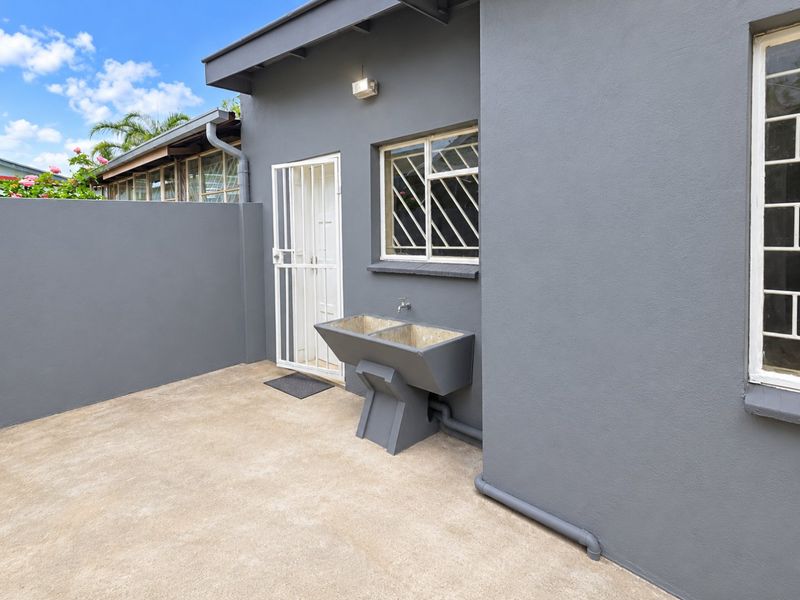 Rear exterior area featuring a concrete laundry trough, security gate, and security bars on windows, set against a painted boundary wall.