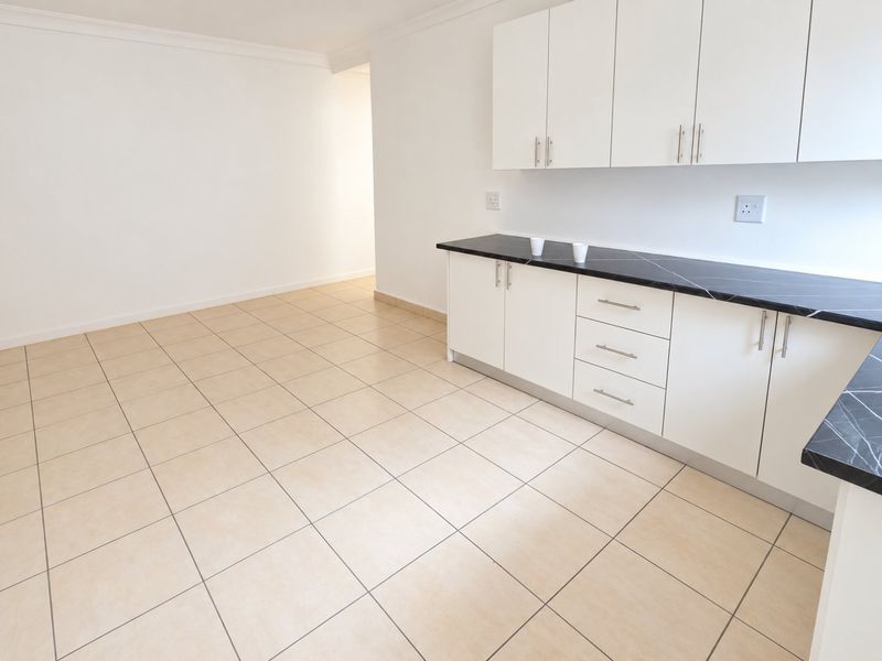 A clean, empty kitchen featuring white cabinetry, black marble-effect countertops, and neutral ceramic floor tiles.