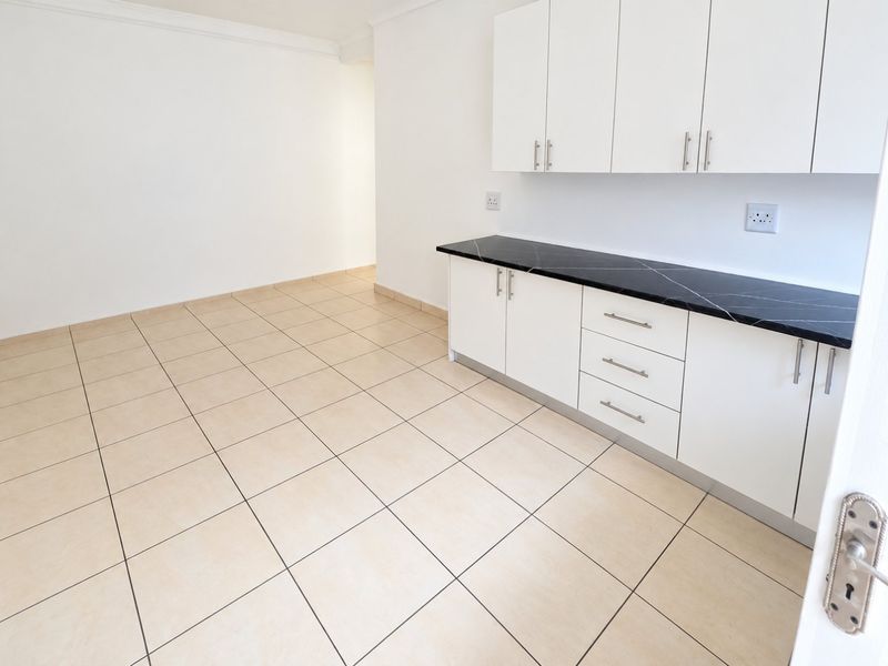 A clean, empty kitchen area featuring white built-in cabinetry, a dark stone countertop, and neutral tiled flooring.