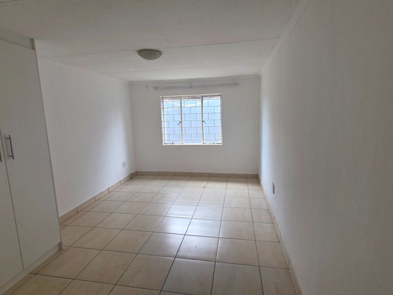 A clean, empty bedroom featuring neutral tiled flooring and built-in cupboards, offering a blank canvas for personalization.