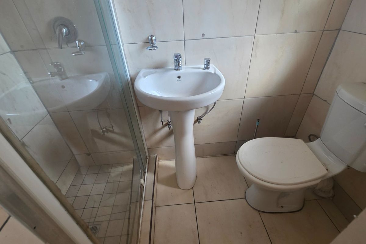 A functional bathroom featuring a pedestal basin, toilet, and a glass-enclosed shower with neutral wall and floor tiling.