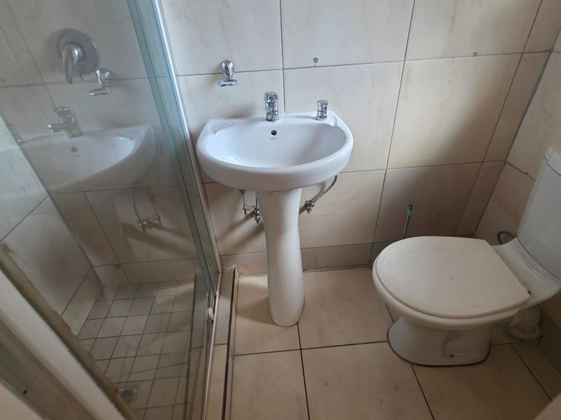 A functional bathroom featuring a pedestal basin, toilet, and a glass-enclosed shower with neutral wall and floor tiling.